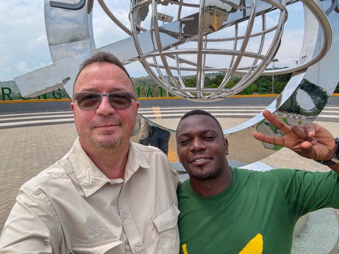 Two men pose by a globe sculpture in Uganda. Peace sign.