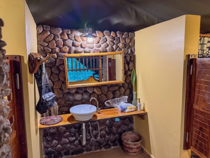 Rustic bathroom interior with stone wall, wooden sink counter, and round vessel sink.