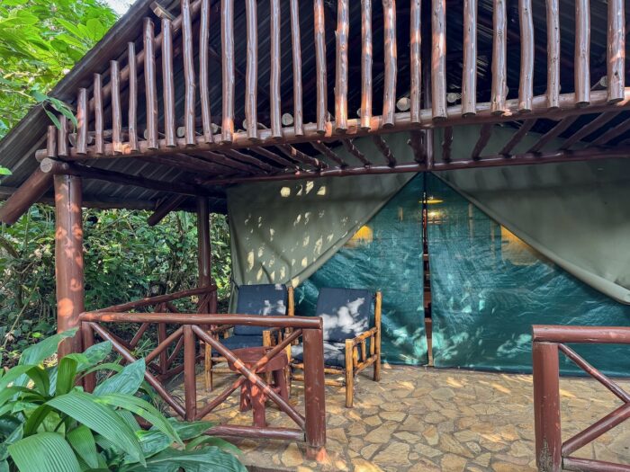 Lodge tent with patio in Uganda, featuring wooden chairs and stone floor.