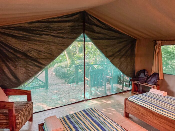 Luxury safari tent interior with bed, chairs, and view of Uganda landscape.
