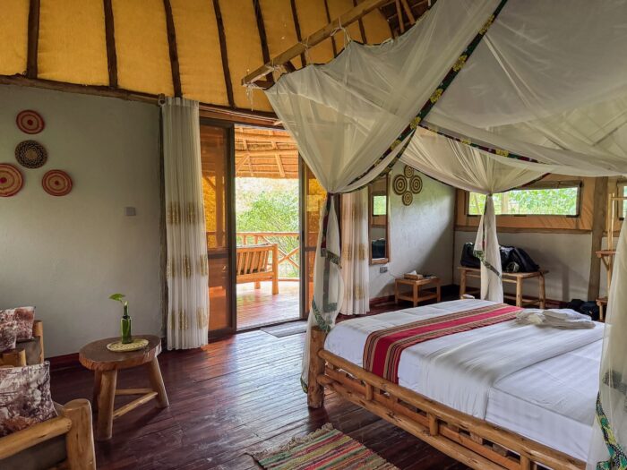 Ugandan lodge bedroom with canopy bed and balcony overlooking lush greenery.