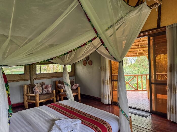 Ugandan lodge bedroom with mosquito net, wood furniture, and balcony view. Uganda travel.