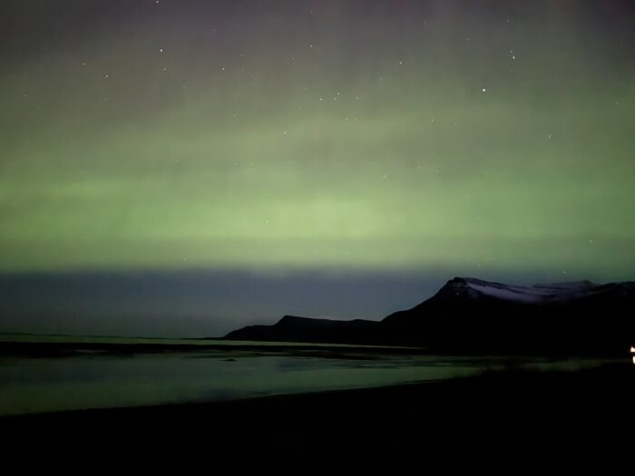 Aurora Borealis over Icelandic mountains and water. Green and purple sky with stars.