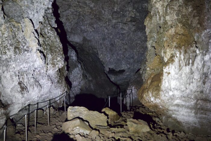 Cave interior with metal railing, rough rock walls, and rocky floor.