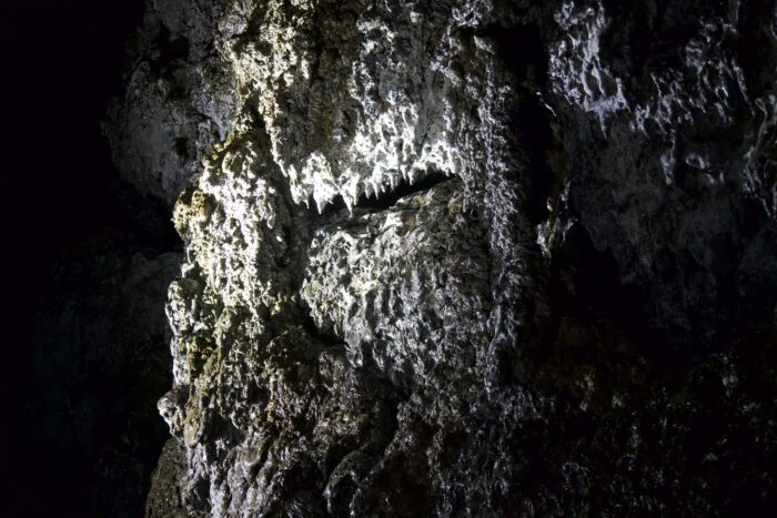 Cave rock formation with textured surface and light shining on it.