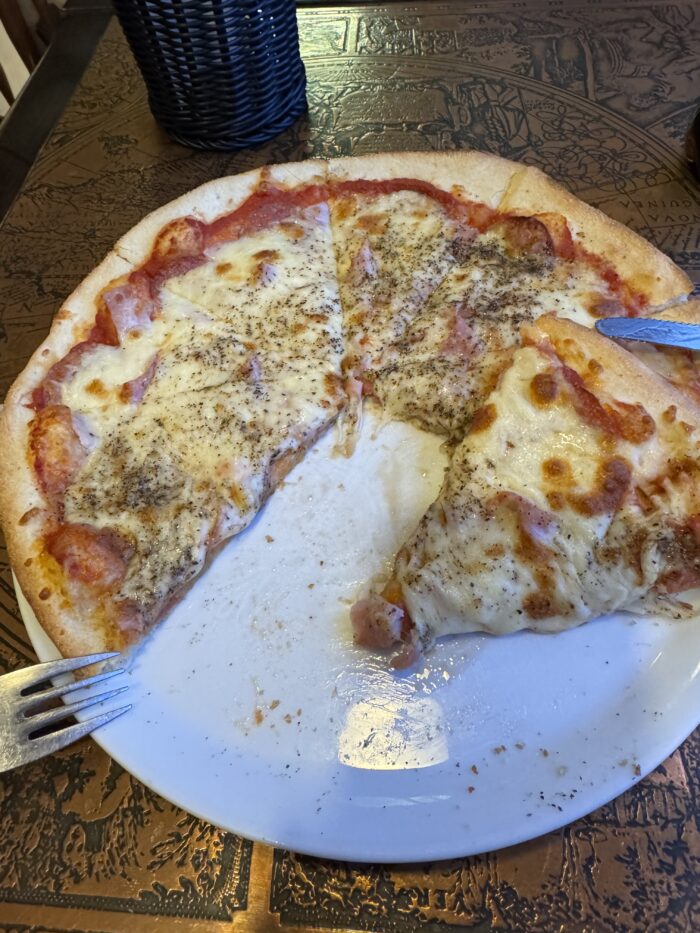 Pizza with ham and cheese on a white plate, ready to eat.