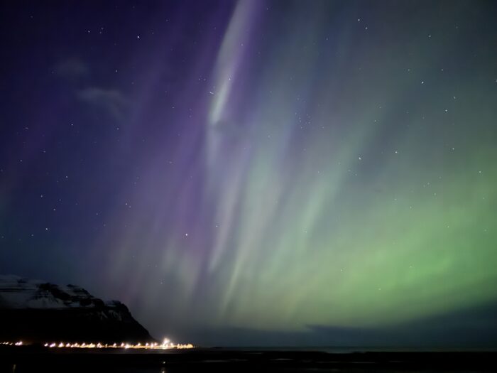 Aurora borealis over Iceland coast with mountains and lights. Purple and green northern lights display.
