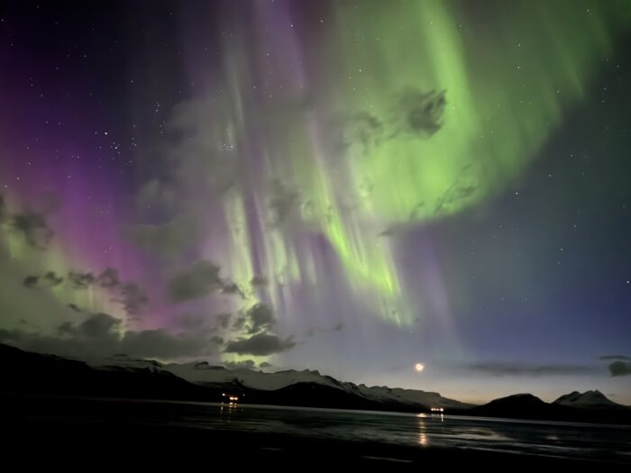 Aurora Borealis over Iceland mountains. Green and purple Northern Lights display. Stars visible in the night sky.