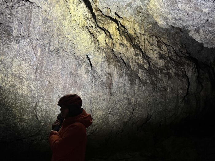 Person exploring a cave in Iceland with headlamp, rocky walls.
