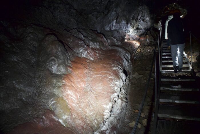 Person descending stairs in a cave with red rock formations, Iceland.