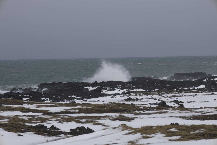 Icelandic coast with waves crashing on black lava rocks, snow patches