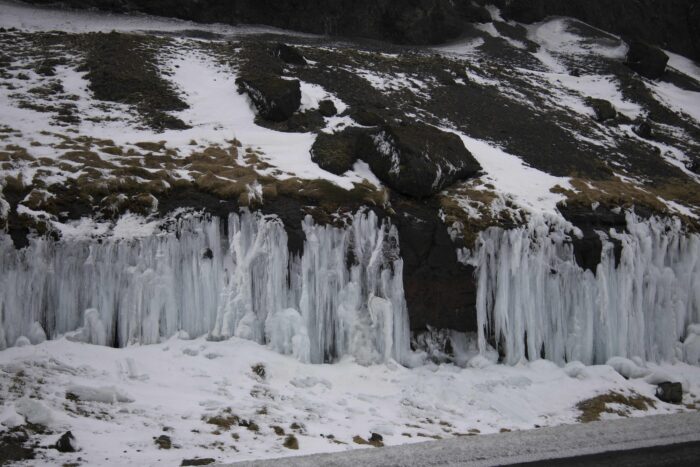 Frozen waterfall in Iceland with snow and rocks, forming ice columns.
