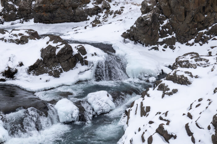 Frozen waterfall and river in a snowy, rocky landscape in Iceland.