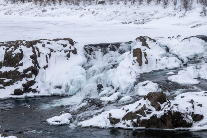 Frozen waterfall cascading over snow-covered rocks in a winter landscape.